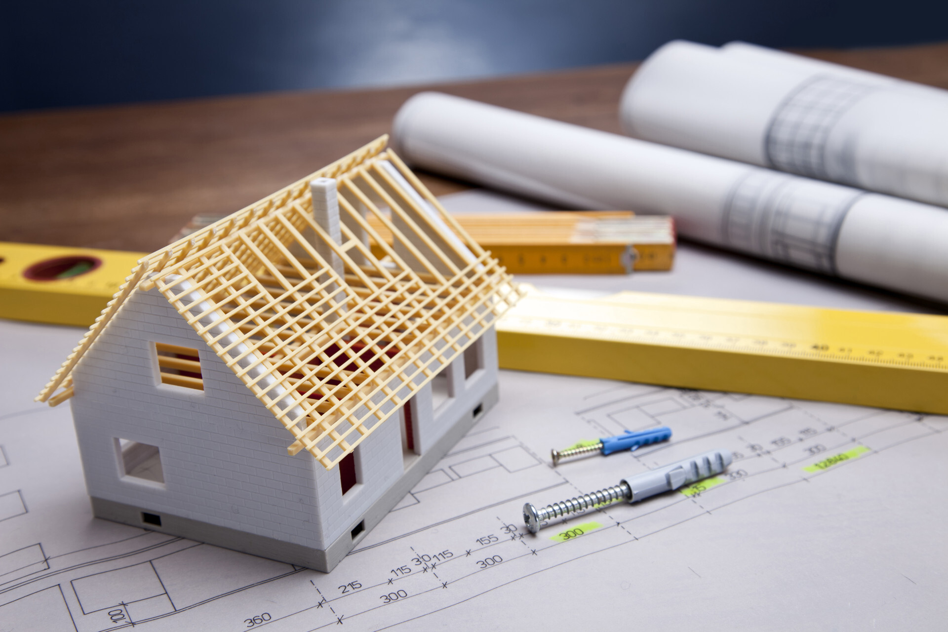 Model house resting on top of blueprints surrounded by level and screws